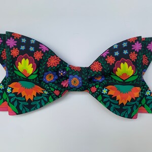 May include: A black bow tie with a colorful floral pattern. The pattern features red, orange, yellow, green, blue, and purple flowers on a black background.