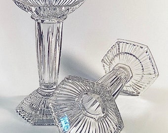 May include: Two clear glass candle holders with a hexagonal base and a fluted design. The candle holders are made of crystal and have a classic, elegant style.
