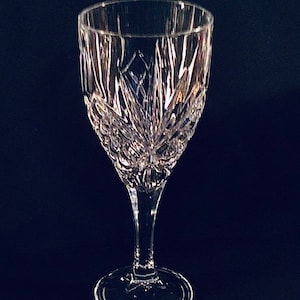 Può includere: Un bicchiere da vino in vetro trasparente con un design in cristallo tagliato. Il bicchiere ha un gambo alto e una base rotonda.