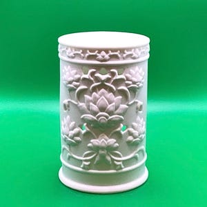May include: A white, cylindrical container with intricate floral relief carvings. The design features lotus flowers and decorative patterns around the top and bottom. The container is made of a solid, opaque material.