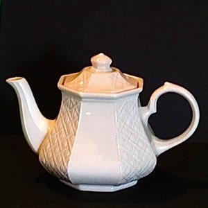 May include: White ceramic teapot with a geometric design and a lid. The teapot has a handle and a spout.