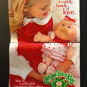 Puede incluir: Una muñeca Cabbage Patch Kids con un vestido blanco con corazones rojos y un lazo rojo en el pelo. La muñeca está siendo sostenida por una niña que lleva un vestido rojo con un cuello blanco y una diadema roja. La imagen tiene el texto "adopt a cuddly bundle of love." y "Now in a collectible Valentine's Day edition designed exclusively for Avon. See next page."