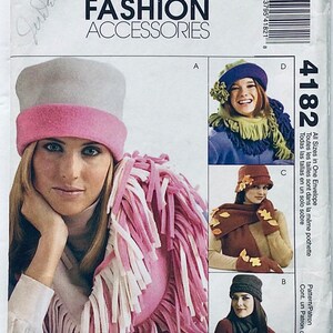 Könnte beinhalten: Ein Schnittmuster für vier verschiedene Winteraccessoires. Das Muster beinhaltet einen Hut mit einem rosa und weißen Fransenbesatz, einen Hut mit einem braunen Fransenbesatz, einen Hut mit einem blauen und grünen Fransenbesatz und einen Hut mit einem grauen Fransenbesatz. Das Muster heißt "McCall's Fashion Accessories" und die Musternummer ist 4182.