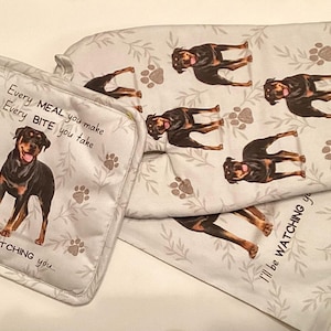 May include: A white kitchen set featuring a Rottweiler dog design. The set includes a pot holder with the text "Every MEAL you make, Every BITE you take, I'll be WATCHING you..." and a matching oven mitt and towel.