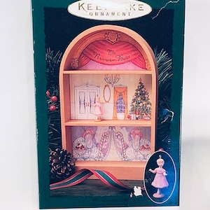 Könnte beinhalten: Eine grüne Box mit einem weißen und goldenen Etikett, auf dem "Keepsake Ornament" steht. Die Box zeigt eine Miniatur-Holzbühne mit einer Ballerina-Figur und einem Weihnachtsbaum. Der Text "The Nutcracker Ballet" ist auf der Bühne gedruckt. Die Box ist Teil einer "Neuen Sammleredition".