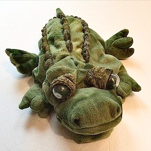 May include: Green plush alligator puppet with large, black eyes and a textured back. The puppet is designed for hand use and has a wide open mouth.