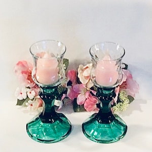 Könnte beinhalten: Ein Paar grüne Kerzenhalter aus Glas mit klaren Glaskerzenbehältern und rosa Kerzen. Die Kerzenhalter haben ein geriffeltes Design und sind perfekt, um jedem Zuhause einen Hauch von Eleganz zu verleihen.