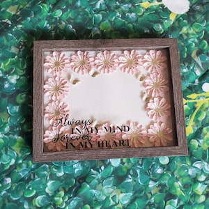 May include: A framed shadow box with a white background and a pink and gold floral border. The text "Always in my mind forever in my heart" is printed in black on the white background.