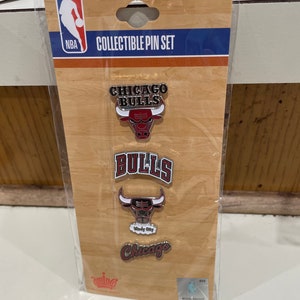 May include: A collectible pin set featuring the Chicago Bulls logo and team name. The pins are displayed on a wooden-textured backing with the NBA logo and the text "COLLECTIBLE PIN SET". The pins include the team's bull logo and the words "Chicago" and "Bulls".