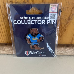May include: Officially licensed UCLA collector pin featuring a cartoon bear wearing a blue and gold jersey with the word "UCLA" on it. The pin is on a blue background with the words "Officially Licensed Collector Pin" and "WinCraft by Fanatics" printed on it.
