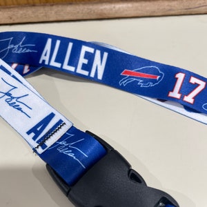 Puede incluir: Un cord&oacute;n azul y blanco con el nombre "ALLEN" y el n&uacute;mero "17" impreso en &eacute;l. El cord&oacute;n tiene un clip de pl&aacute;stico negro.