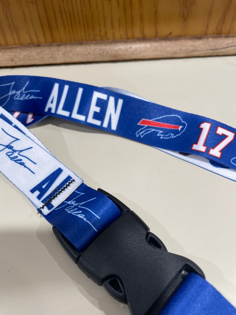 Puede incluir: Un cord&oacute;n azul y blanco con el nombre "ALLEN" y el n&uacute;mero "17" impreso en &eacute;l. El cord&oacute;n tiene un clip de pl&aacute;stico negro.