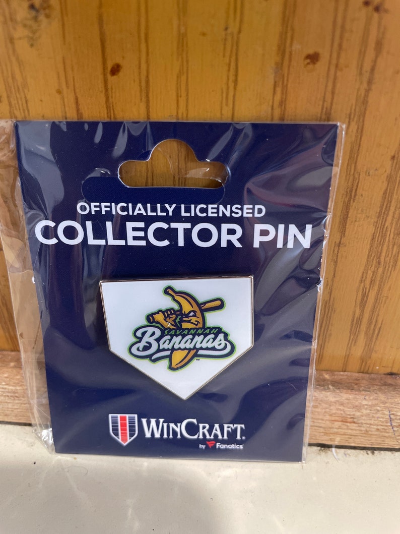 May include: Officially licensed collector pin featuring a white baseball home plate with a yellow banana holding a bat and the text "Savannah Bananas". The pin is packaged on a blue card with the WinCraft logo and the text "by Fanatics".