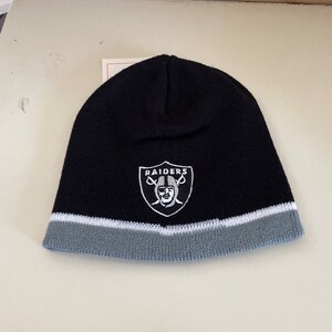 May include: Black knit beanie with a gray brim and a white embroidered Raiders logo featuring a skull and crossbones.