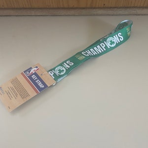 May include: Green key strap with "2022 NBA CHAMPIONS" text and the Boston Celtics logo. The key strap has a white and green design. A brown and white tag reads "KEY STRAP" and features the NBA logo.