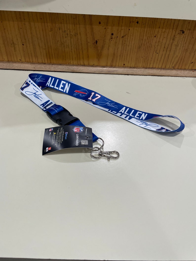Puede incluir: Un cord&oacute;n azul y blanco con el nombre "Josh Allen" y el n&uacute;mero "17" impreso en &eacute;l. El cord&oacute;n tiene un clip negro y un llavero plateado.