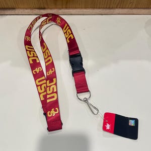 May include: Red lanyard with the text "USC" in yellow. The lanyard has a black plastic clasp and a metal clip. A black and red tag is attached to the clip.