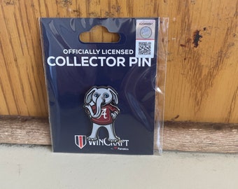 Puede incluir: Pin de coleccionista con licencia oficial que presenta un elefante de dibujos animados con una camiseta roja y blanca de Alabama Crimson Tide con la letra "A" en la parte delantera. El pin está sobre un fondo azul con las palabras "Officially Licensed Collector Pin" y "WinCraft by Fanatics" impresas en él.