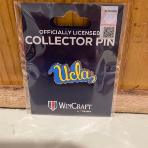 May include: A blue and yellow UCLA logo collector pin on a black background with the text "Officially Licensed Collector Pin" and "WinCraft by Fanatics".