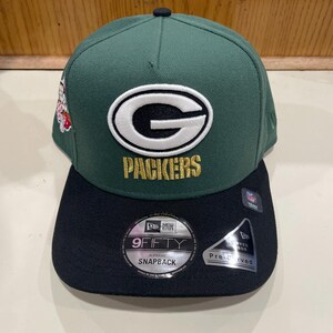 May include: Green and black snapback hat with the Packers logo. The hat features a green crown and a black brim. The Packers logo is white with a black outline and the word "PACKERS" in gold lettering. The hat has a "9FIFTY" sticker.
