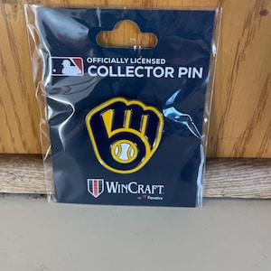 May include: A collector pin featuring a baseball glove design with a baseball in the center. The pin is yellow and navy blue, and is packaged in a clear plastic sleeve. The packaging includes the text "OFFICIALLY LICENSED COLLECTOR PIN" and the WinCraft logo.