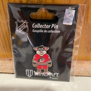 May include: A Carolina Hurricanes mascot collector pin featuring a brown-furred character wearing a red hockey jersey with the number 9 on the sleeve and the team logo on the chest. The pin is sealed in original black packaging with NHL branding.