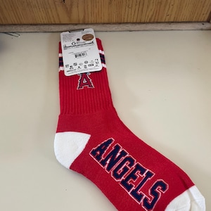 May include: Red and white crew socks with blue lettering that says "ANGELS". The socks have a white stripe with a blue stripe above it. The socks also have a red "A" on the front.