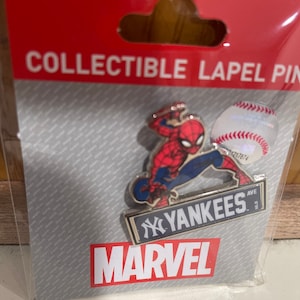 May include: A collectible lapel pin featuring Spider-Man in a red and blue suit, holding a baseball. The pin also includes a blue and white sign with the text "Yankees" and the Marvel logo.
