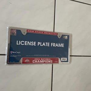 May include: A silver license plate frame with the text "Ohio State Buckeyes" and "License Plate Frame". The frame also features the text "2024 National Champions" with a red and white Ohio State logo.