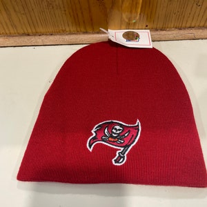 May include: Red knit beanie with a white embroidered Tampa Bay Buccaneers logo featuring a skull and crossbones.