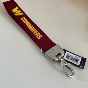 May include: A burgundy red key chain with a gold W and the word "COMMANDERS" in gold lettering. The key chain has a silver metal clasp.