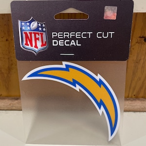 May include: A Perfect Cut decal featuring the NFL logo and the Los Angeles Chargers logo, a blue and yellow lightning bolt. The decal is packaged in a clear plastic sleeve with a black backing that reads "PERFECT CUT DECAL".