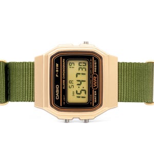 May include: A gold-tone Casio F-91W digital watch with a green nylon strap. The watch face displays the time, date, and day of the week. The watch is water resistant.