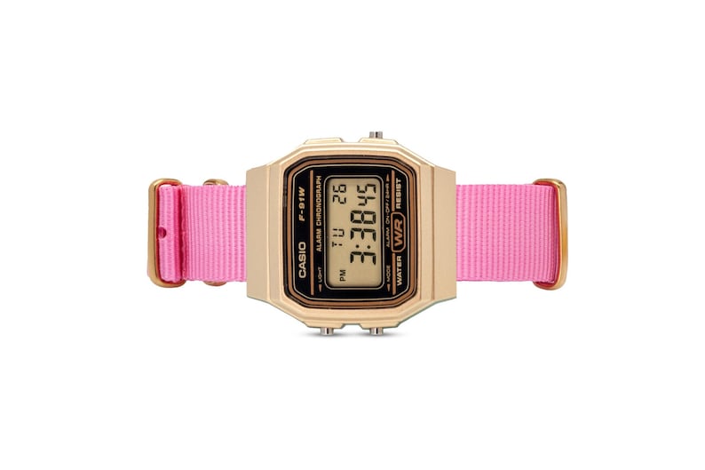 Puede incluir: Un reloj digital Casio de color dorado con una correa de nailon rosa. La esfera del reloj muestra la hora, la fecha y el d&iacute;a de la semana. El reloj es resistente al agua.