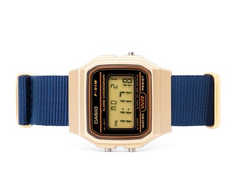 May include: A gold Casio F-91W digital watch with a blue nylon strap. The watch face displays the time, date, and day of the week. The watch is water resistant.