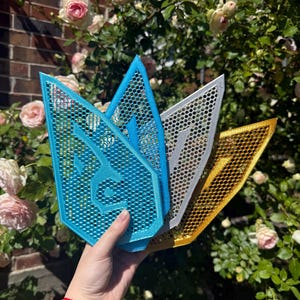 Pode incluir: Três painéis decorativos de parede em forma de seta estilizada. Os painéis são feitos de um material de malha e são de cor azul, prata e dourado.