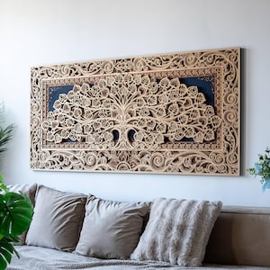 Könnte beinhalten: Ein großes, rechteckiges Wandkunstwerk aus Holz mit einem detaillierten Baumdesign. Das Kunstwerk ist aufwendig mit einer hellbraunen Oberfläche geschnitzt, vor einem dunkelblauen Hintergrund. Der Rahmen hat verzierte Schnörkel. Es hängt über einem Sofa.