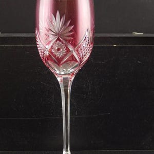 Könnte beinhalten: Ein klares Weinglas mit geschnittenem Kristallmuster. Das Glas hat eine rosafarbene Tönung und einen langen, schlanken Stiel.