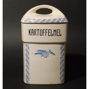 May include: White ceramic canister with a blue and white patterned design. The canister has a lid with a handle and says "KARTOFFELMEL" in black lettering.