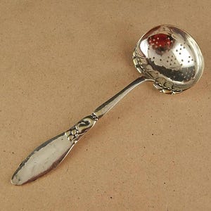 May include: A silver tea strainer with a perforated bowl and a decorative handle. The handle features a floral design.