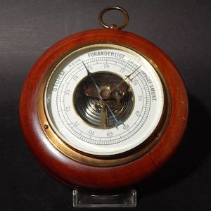 May include: A wooden framed barometer with a brass face and a white dial. The dial has markings for "Storm", "Regn", "Foranderligt", "Smuk", and "Meget Smuk".