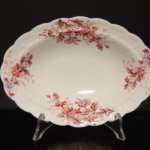 Puede incluir: Plato ovalado blanco para servir con borde festoneado. El plato está decorado con un patrón floral en tonos rojos, rosas y verdes.