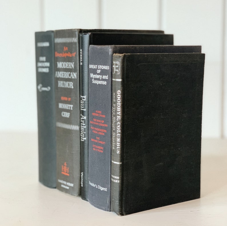 May include: A collection of vintage books with dark gray and black covers. Titles include "Five Detective Stories", "Modern American Humor", "Paul Artleigh", "Great Stories of Mystery and Suspense", and "Goodbye, Columbus". The books are arranged vertically.