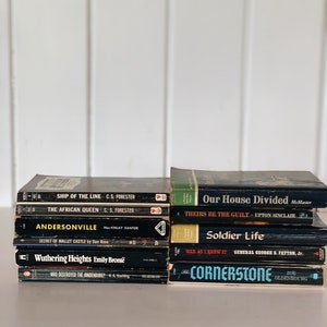 May include: A stack of ten paperback books with black covers and white text. The titles include "Ship of the Line", "The African Queen", "Andersonville", "Secret of Mallet Castle", "Wuthering Heights", "Who Destroyed the Hindenburg?", "Our House Divided", "Theirs Be the Guilt", "Soldier Life", "War as I Knew It", and "The Cornerstone".