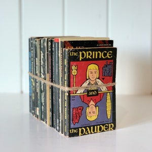Pu&ograve; includere: Una pila di libri tascabili vintage con una copertina nera e rossa che presenta il titolo "Il principe e il povero" di Mark Twain. Il libro fa parte di una serie chiamata "A Logos Book".