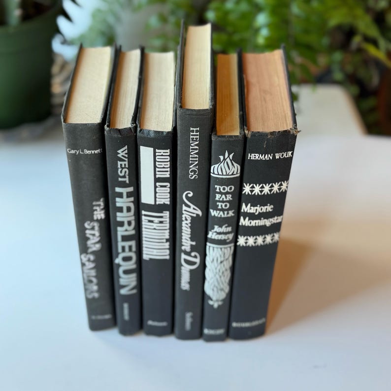 May include: A set of six black hardcover books with white text titles. The titles are "The Star Sailors", "West Harlequin", "Robin Cook Terminal", "Alexandre Dumas", "Too Far To Walk", and "Marjorie Morningstar".