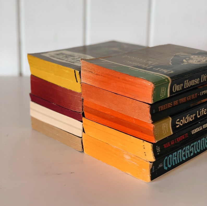 May include: A stack of vintage paperback books with colorful covers. The top book has the title "Our House Divided" and the bottom book has the title "The Cornerstone".