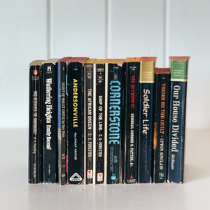 May include: A collection of 12 vintage paperback books with black covers and white text. The titles include "Wuthering Heights", "Andersonville", "The African Queen", "Ship of the Line", "The Cornerstone", "War As I Knew It", "Soldier Life", "Theirs Be The Guilt", and "Our House Divided".