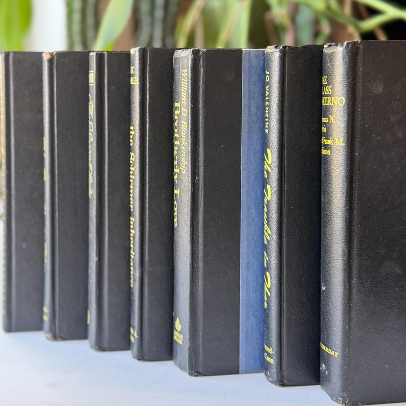 May include: A collection of hardcover books with black spines, some with gold lettering. One book has a blue spine. Titles include "Brotherly Love" and "The Inferno". The books are arranged in a row.