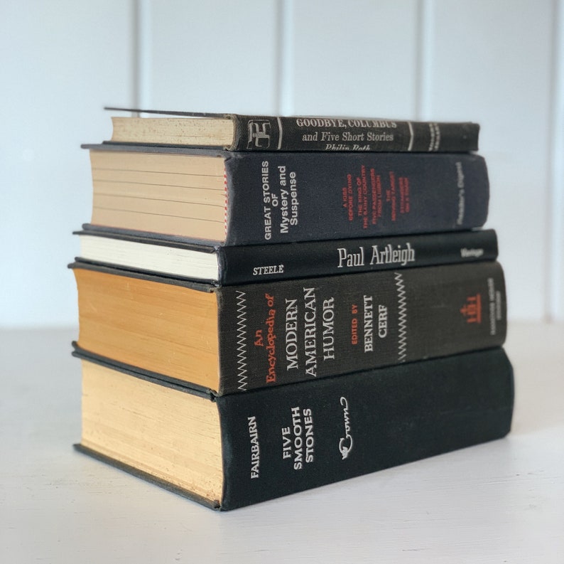 May include: A stack of five hardcover books with black covers and various titles. The books have aged, yellowed pages and are arranged in a neat pile. Titles include "Goodbye, Columbus," "Great Stories of Mystery and Suspense," and "Five Smooth Stones."